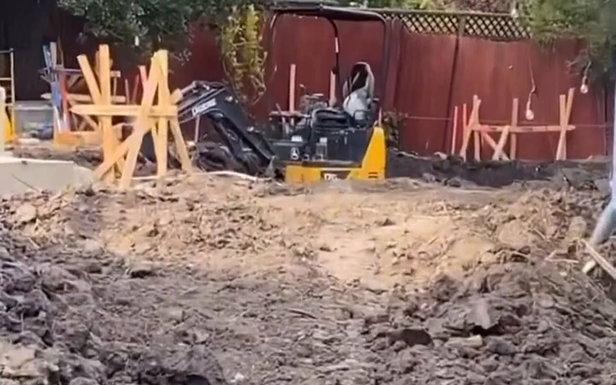 Excavated back yard with soil piles, stakes and braced forms behind a house