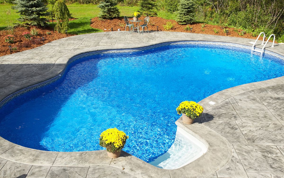 A tiled in-ground pool surrounded by a stamped concrete deck