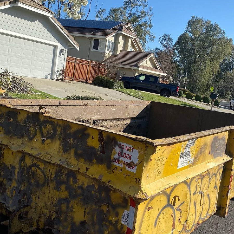 Yellow roll-off container on a residential driveway in front of a garage