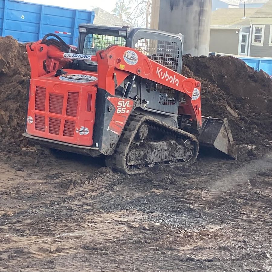 Tracked skid loader working soil between stockpiles and containers