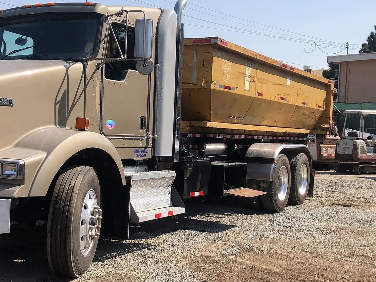 Loaded Kenworth dump truck parked beside a tracked excavator at the BR Services yard