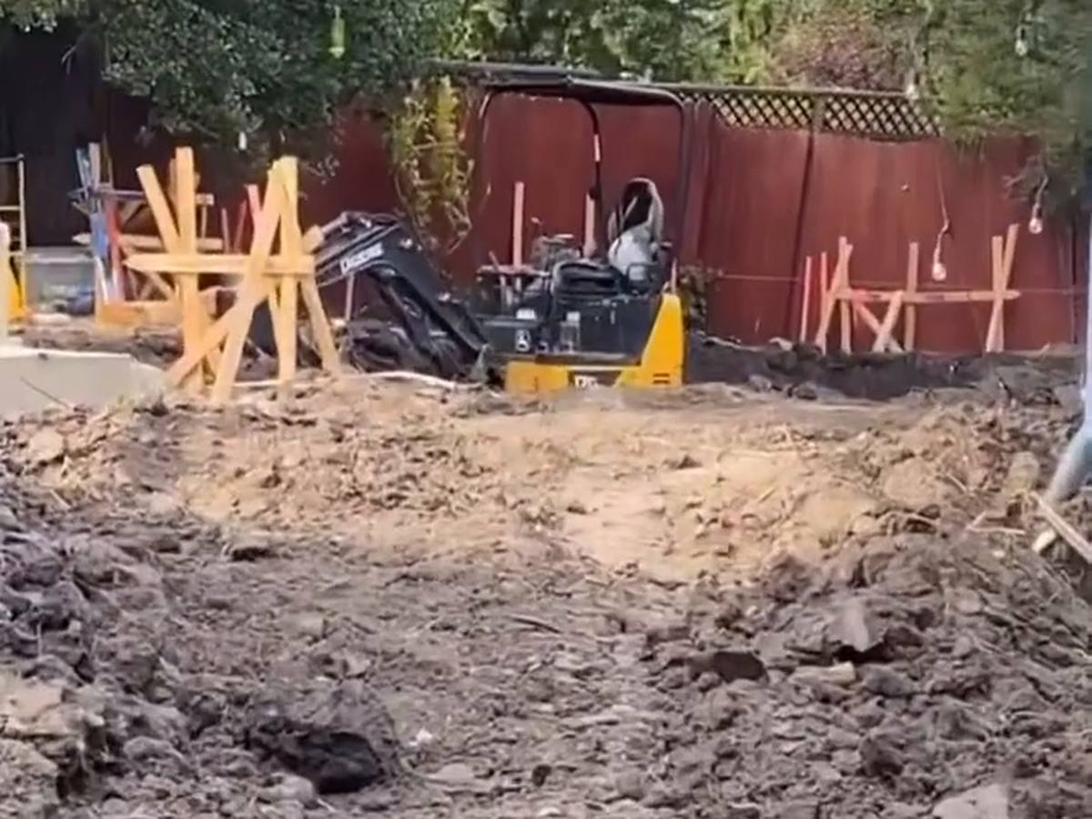 Excavated back yard with soil piles, layout stakes and braced forms behind a house