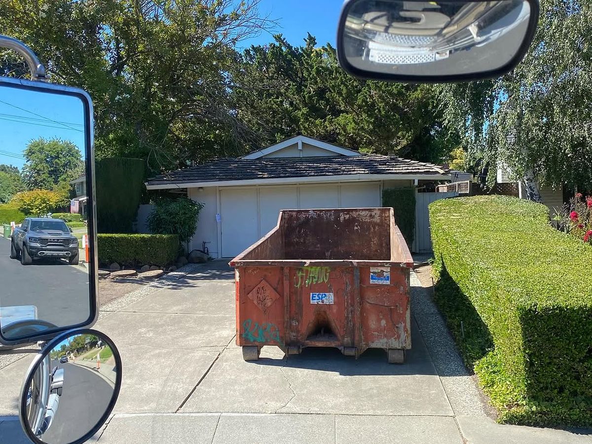 A delivered roll-off container on a residential driveway, seen from the truck cab