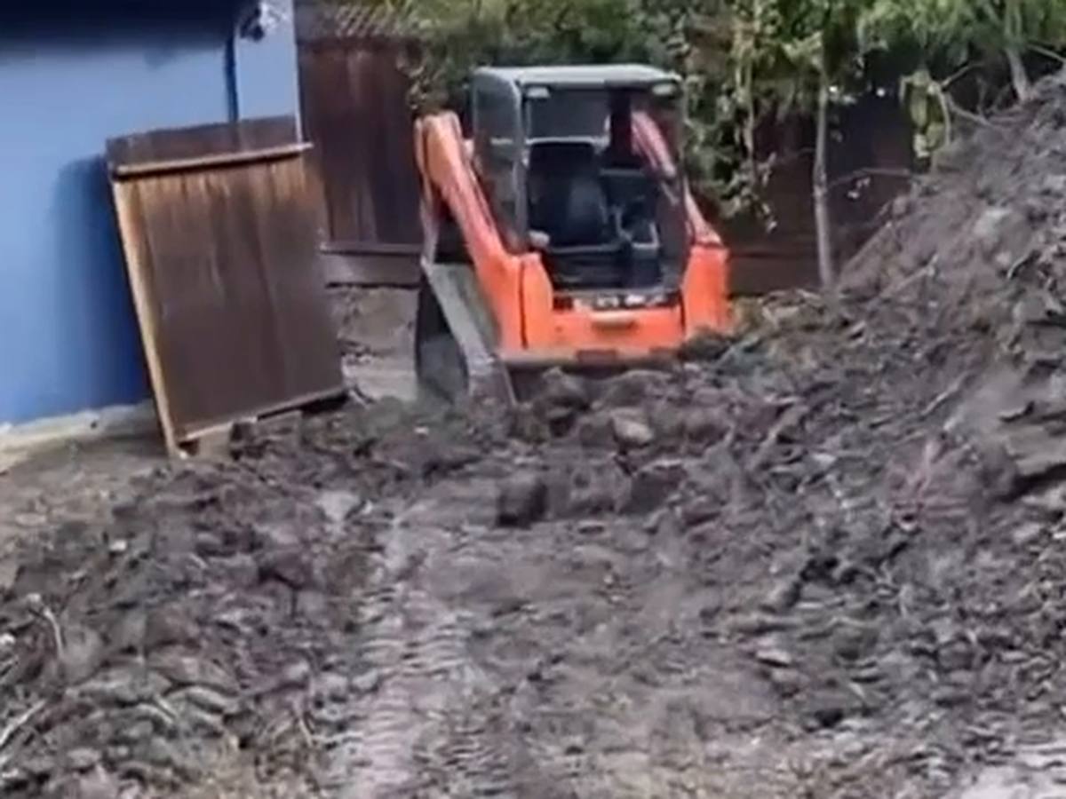 Tracked loader cutting into a soil bank beside a house