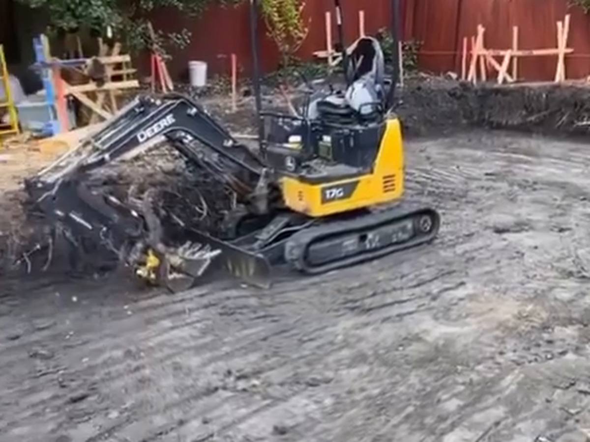 Compact tracked excavator working a cut pad in a fenced back yard