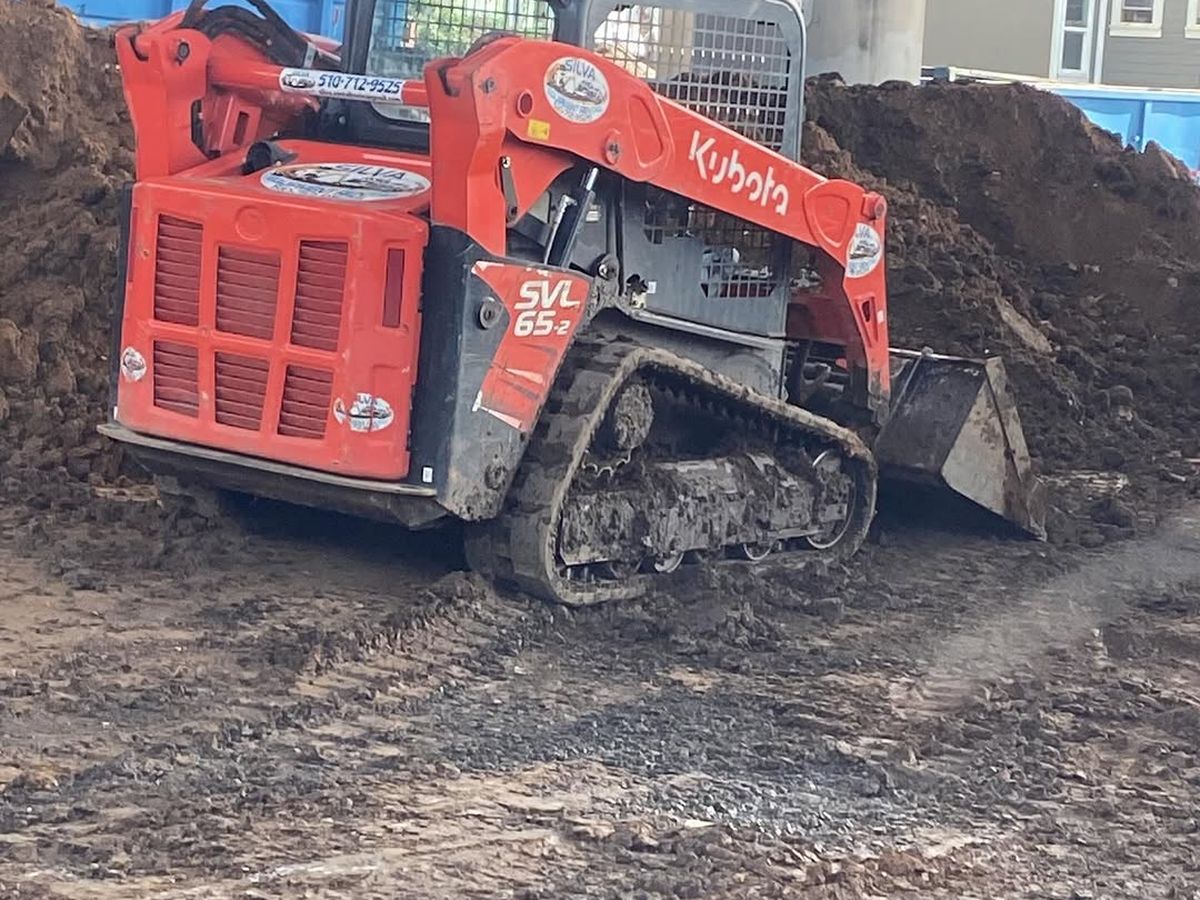 Excavated soil stockpiled on site while a tracked loader works the cut
