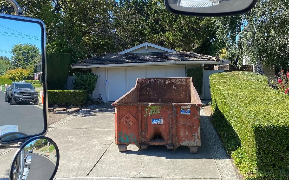 Roll-off container set square on a driveway, photographed through the truck windscreen