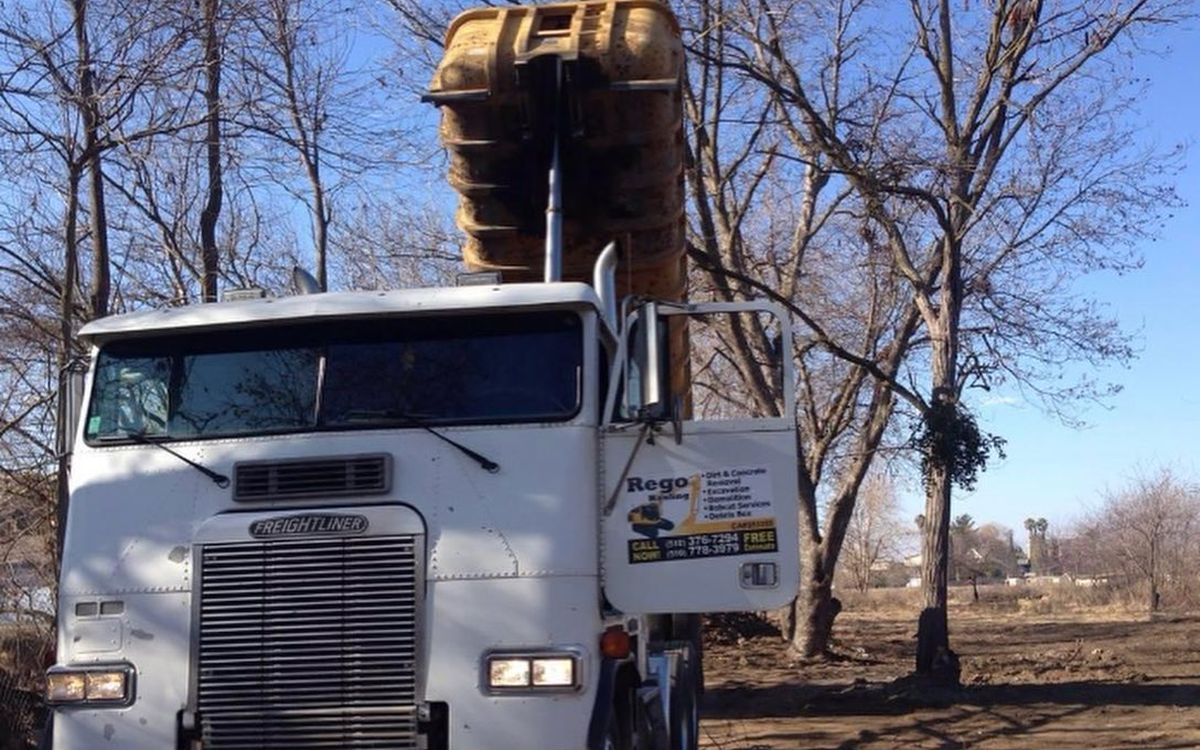 Cab-over Freightliner loaded with a tracked excavator on a cleared lot