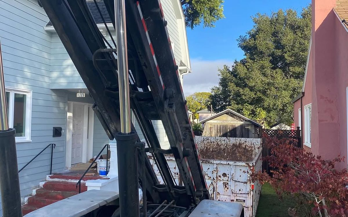 Roll-off truck with the hoist raised, lowering a container into a narrow side yard